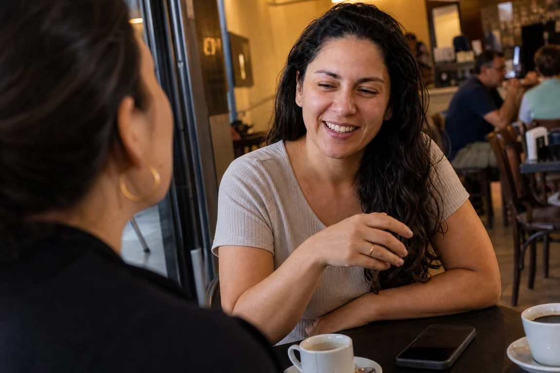 Mulher conversando e rindo com uma amiga em uma cafeteria